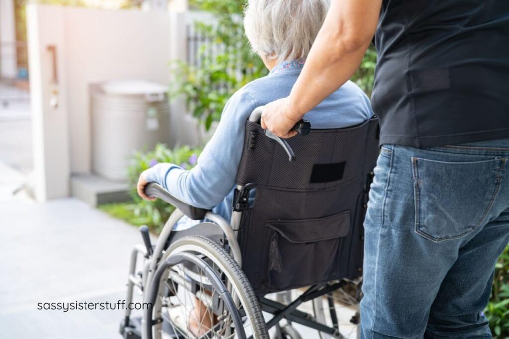 an adult son pushes his mother in a wheelchair down the sidewalk for a spring walk.