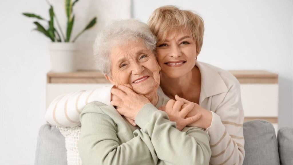 senior woman and her adult daughter snuggle together and smile.