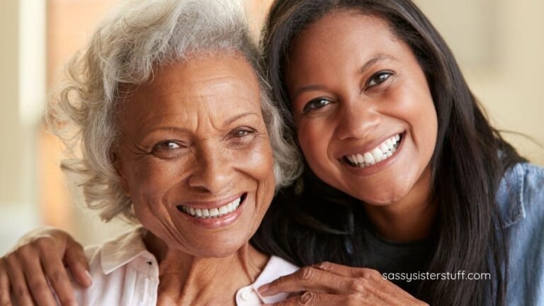 an elderly mother and her adult daughter with their heads together smiling at the camera.