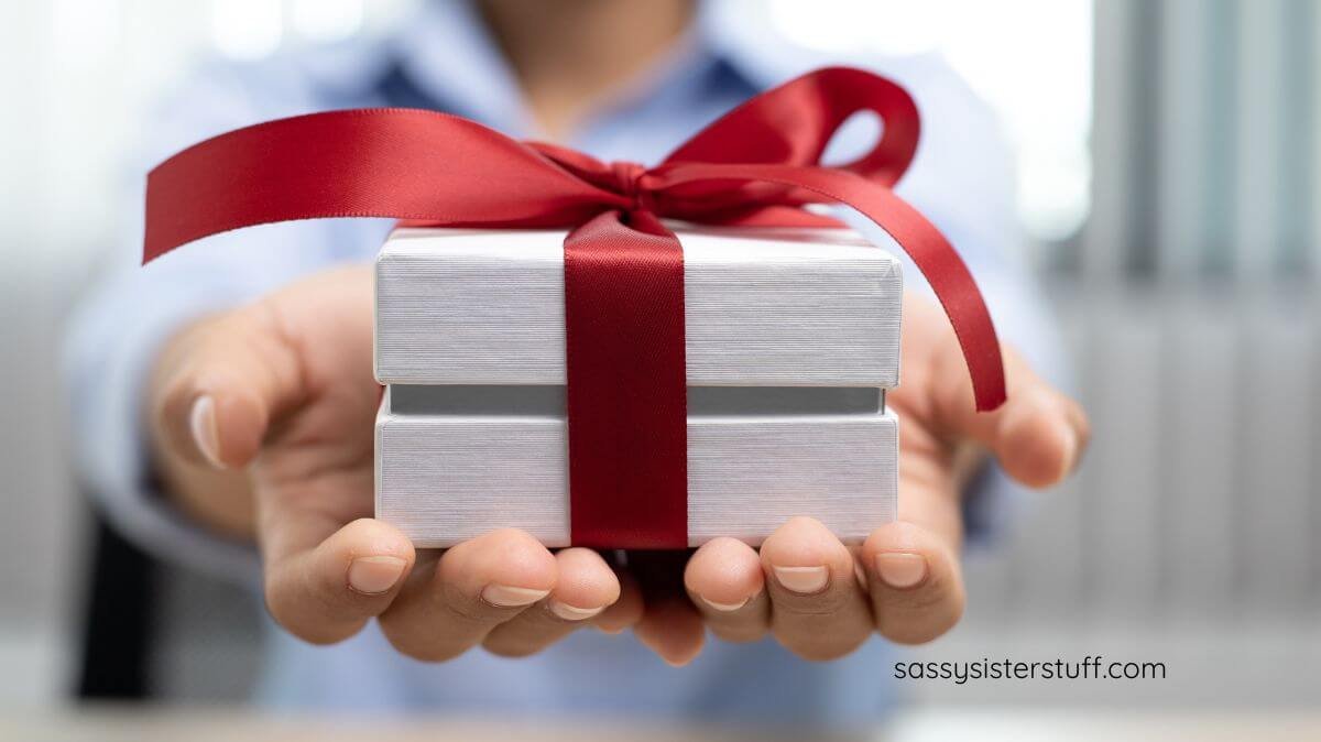 close-up of woman handing someone a gift with a red ribbon.