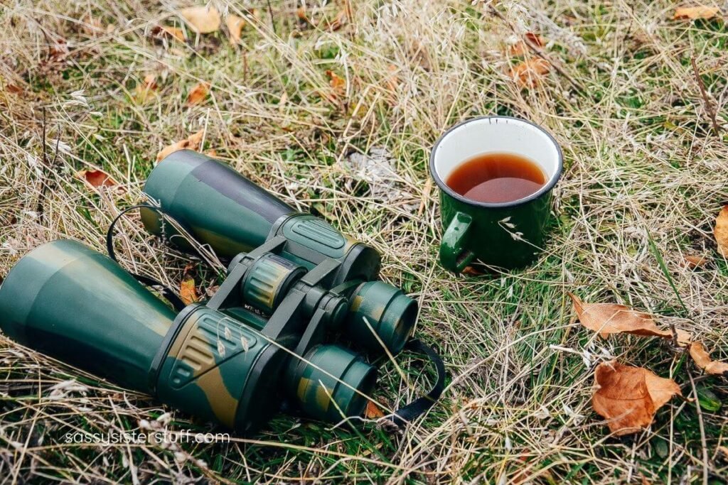 binoculars for bird watching and a cup of tea laying on the ground.