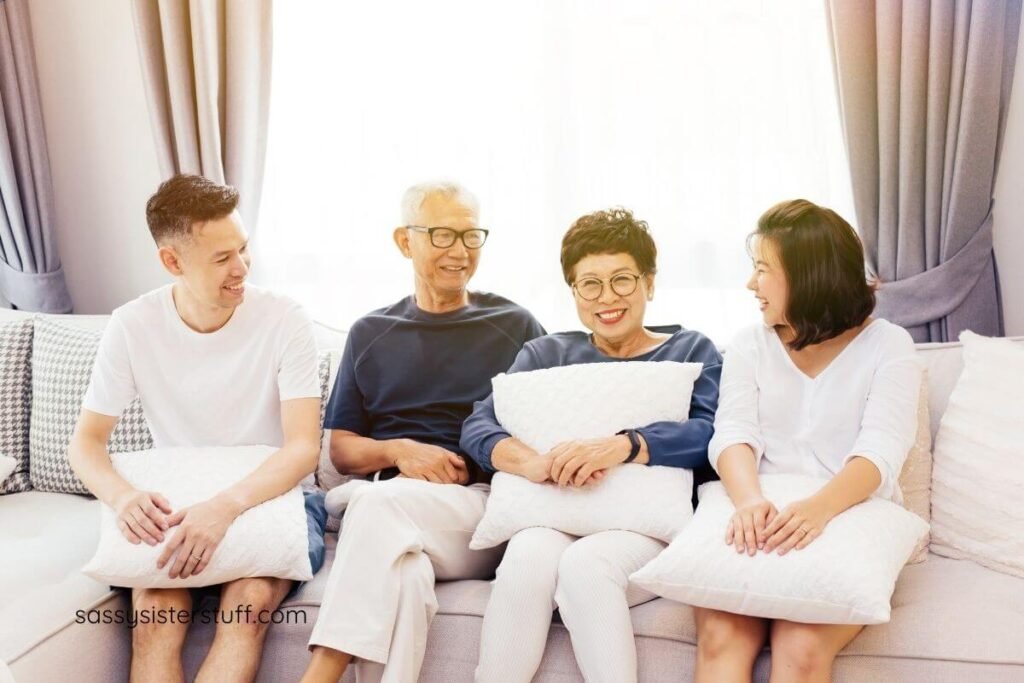 a young Asian couple happily sits on a sofa with their aging parents.