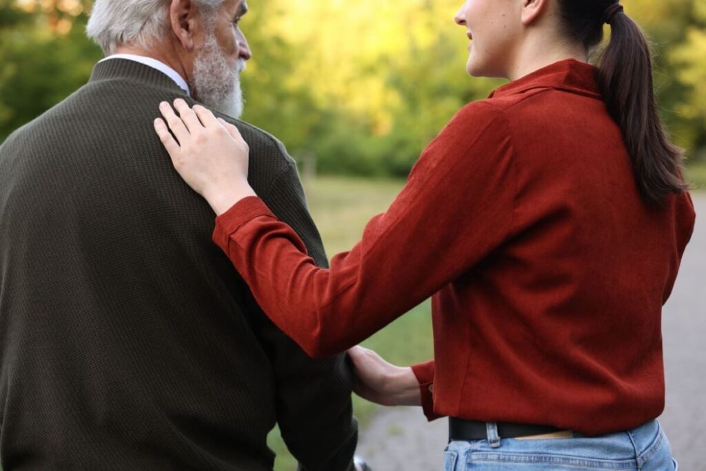 an adult daughter touches her father gently on the shoulder as they begin a walk down the trail.