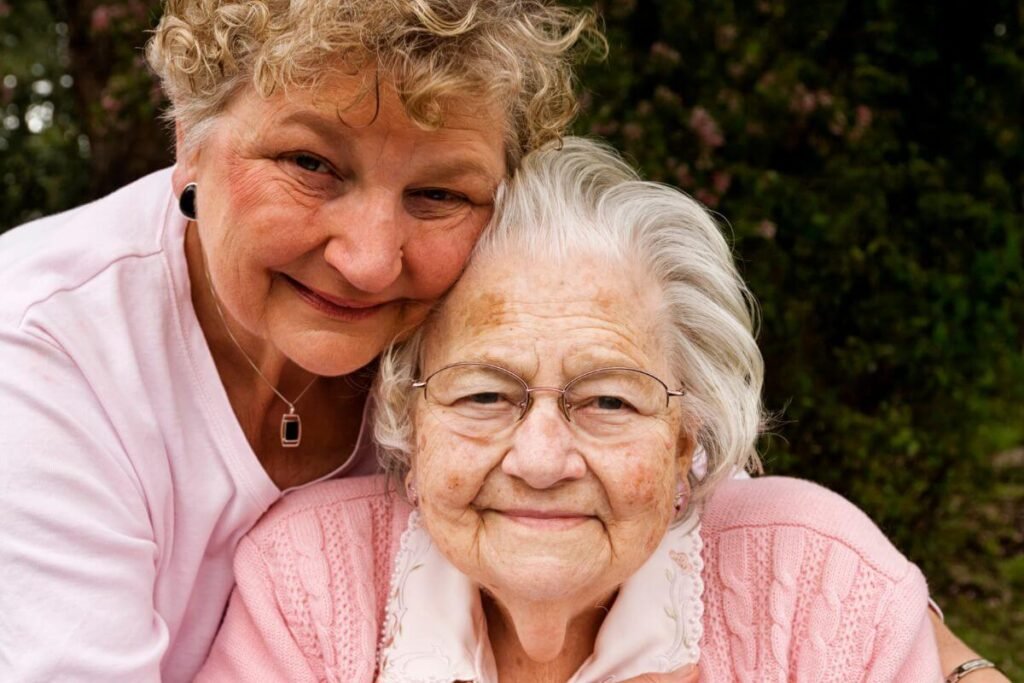 adult daughter hugs her elderly mother from behind.